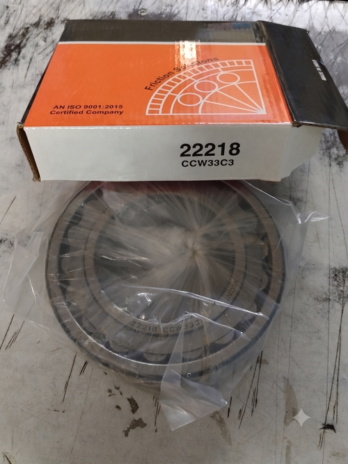 A large circular metal bearing 22218 wrapped in clear plastic sits in front of its box on a worn gray floor.