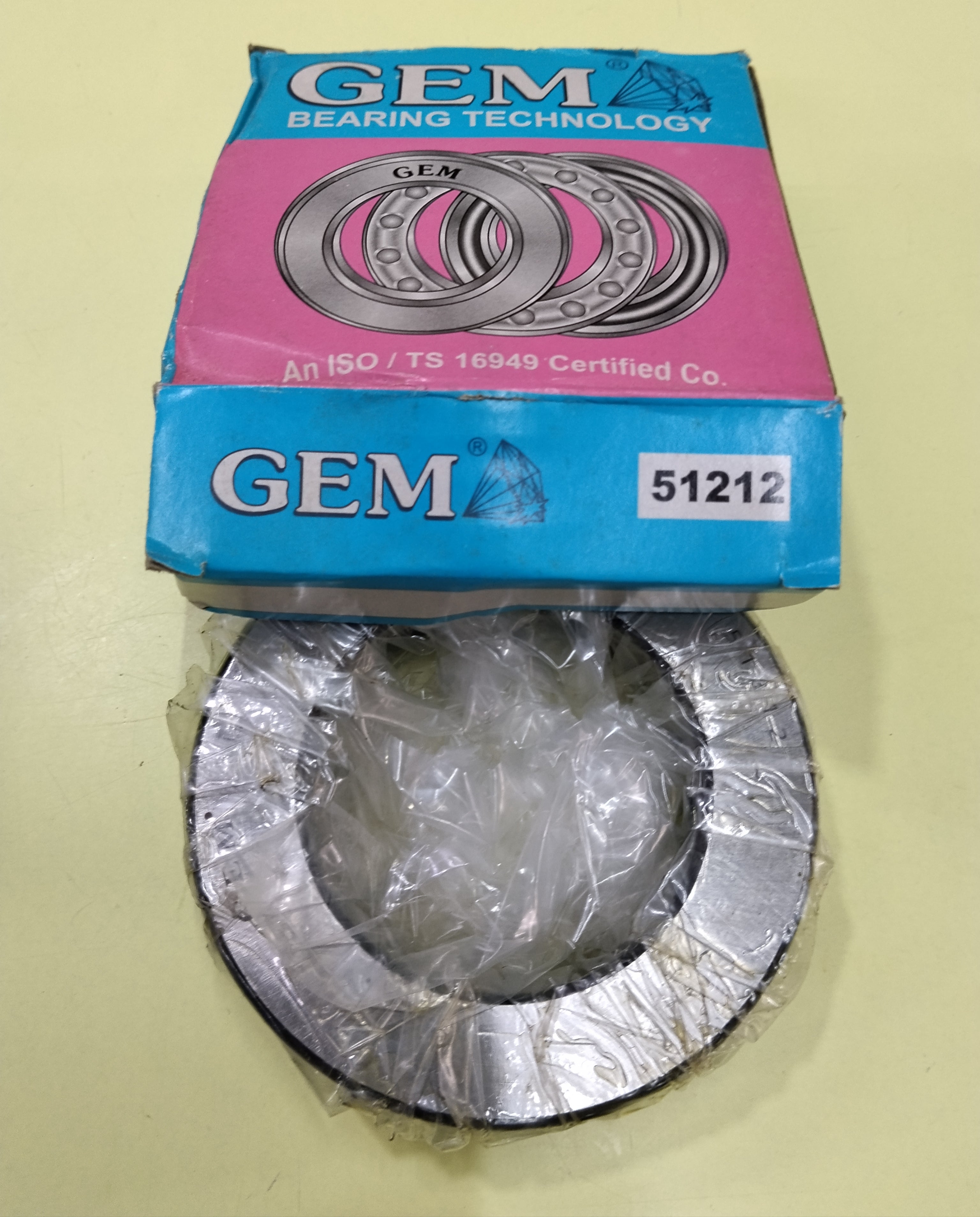 A GEM 51212 THRUST bearing component wrapped in clear plastic, placed below its blue and pink branded cardboard box on a pale yellow background.