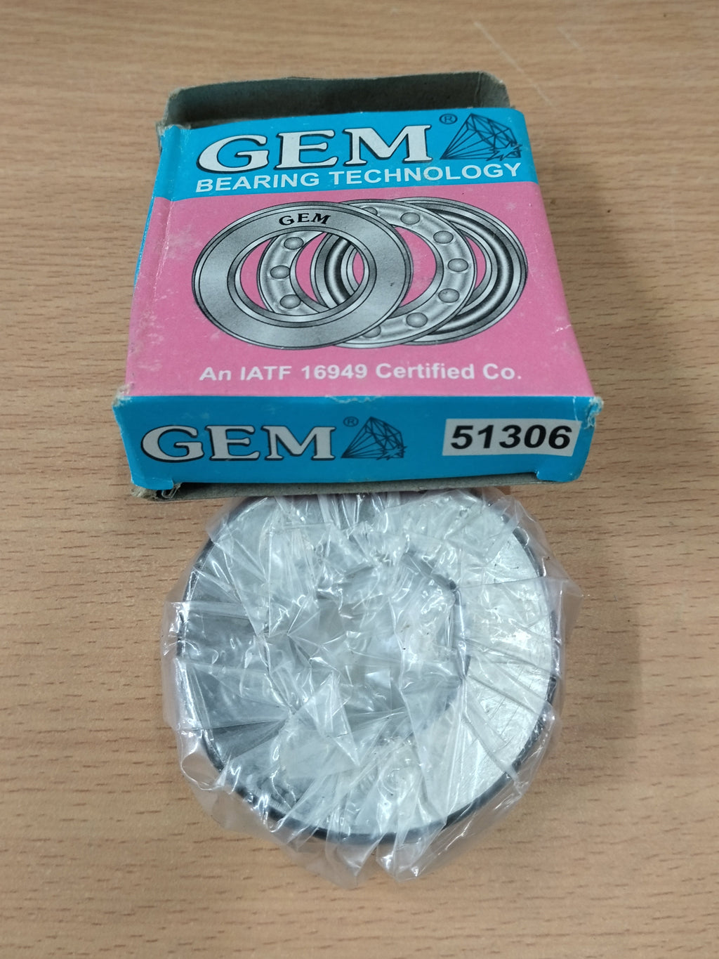A GEM bearing part in clear plastic wrapping placed below its pink and blue retail box on a light wood surface. The box shows the GEM brand and model number 51306.