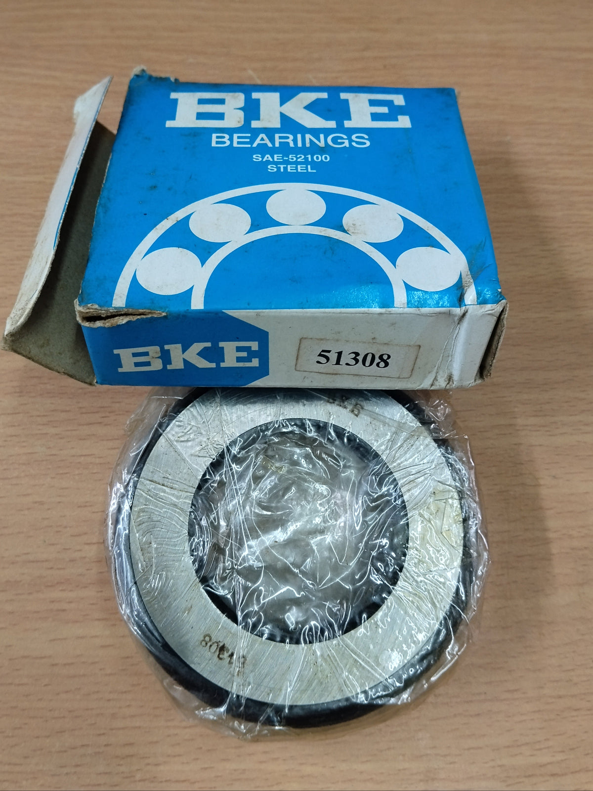 A BKE Bearings steel bearing, model 51308, shown with its original blue cardboard packaging box on a light wood tabletop.