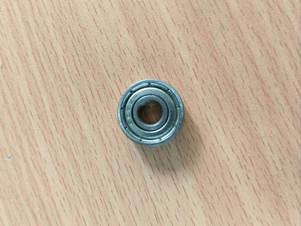 A small miniature metal bearing 608 zz placed on a light wood-grained surface.