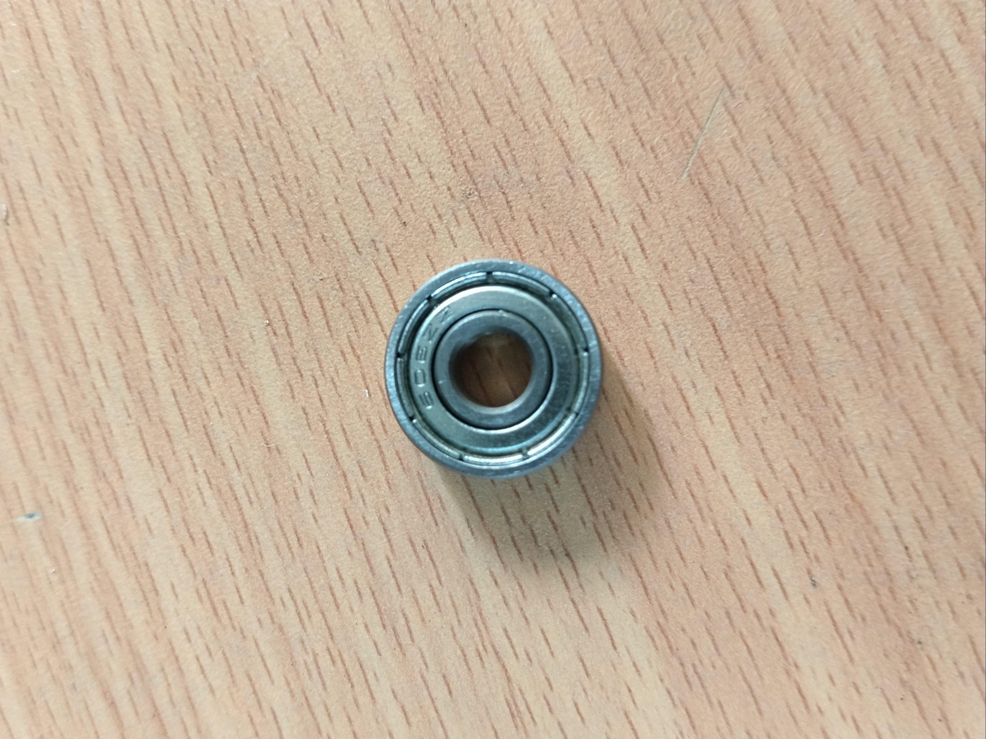 A small miniature metal bearing 608 zz placed on a light wood-grained surface.