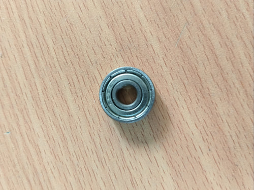 A small miniature metal bearing 608 zz placed on a light wood-grained surface.