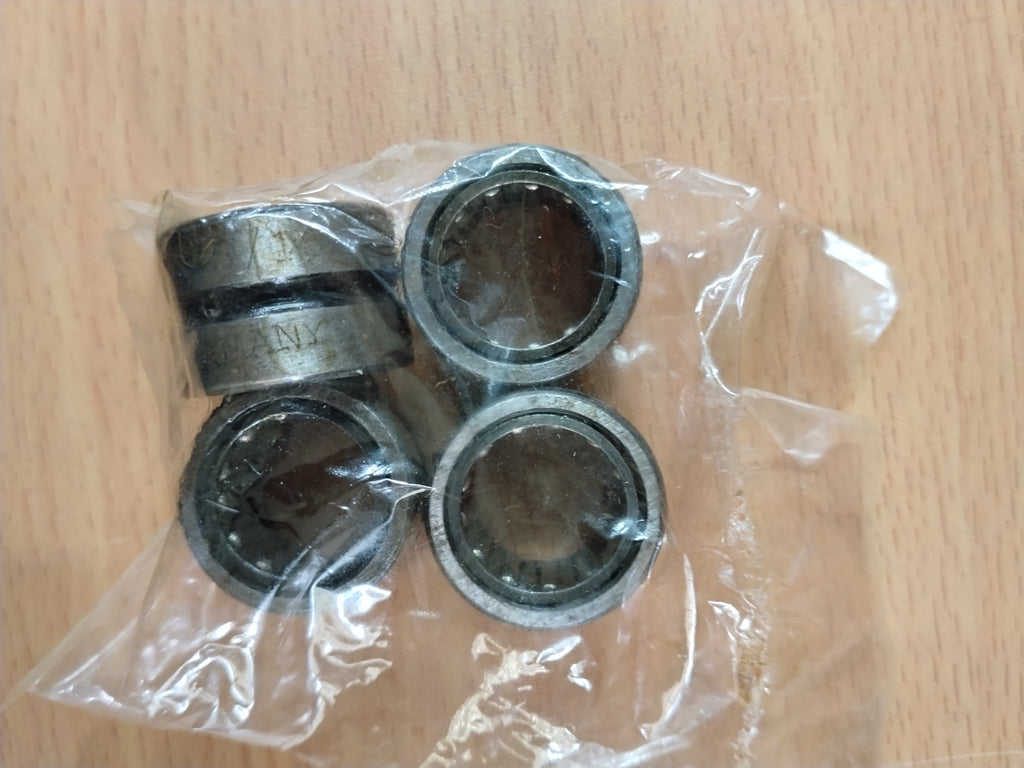 Four metal needle bearings inside a clear plastic bag, placed on a light wood surface.